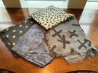 Four pashmina shawls laid flat, showing full variety of color and pattern including animal spots, crosses, stars, and abstract design.