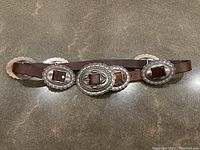 Frontal view of belt laid flat showing all five silver-tone oval conchos on brown leather strap
