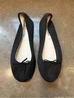 Top down view of pair of black sparkly leather ballet flats with small bows on top.
