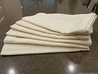 Stack of six off-white cotton napkins folded and stacked on a countertop.