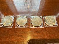 Top view of four silver coins sealed in plastic sleeves placed on wooden surface showing City of Toronto inscriptions and denominations.