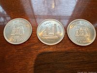 Three silver collectible coins shown side by side on wood surface, showcasing the Coat of Arms and City Hall designs.