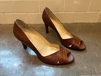 Pair of vintage brown leather peep toe heels by Ralph Lauren, size 9, positioned on a grey countertop against a beige tiled wall, showing right side and top views.