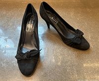 Pair of vintage black suede heels by Saks Fifth Avenue, showing the side and top view of both shoes on a gray surface.