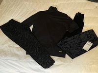 Full view of black short sleeved turtleneck sweater with two pairs of velvet leggings, one patterned and one plain, laid on beige bedspread.