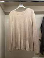 Full view of cream cashmere sweater hanging on hanger showing shape and flared hem.
