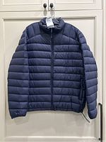 Front view of navy blue Solaris puffer jacket in size XL hanging on white double cabinet doors.