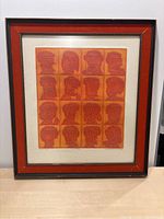 Framed artist proof print showing 16 abstract orange and red faces on a white mat with decorative frame