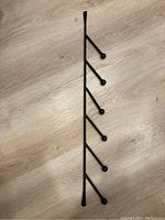 Black metal wall hook system lying flat on a wooden floor, showing five hooks attached vertically.