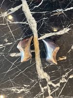 Front view of the pair of sterling silver clip on earrings showing abstract curved design and polished surface on black marble background.