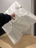 Photo of the white rice paper pendant lamp unfolded, showing its translucent square paper shade with a hand holding the lamp frame.