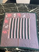 Full view of the scarf laid flat showing floral motif along one edge and striped center panel on muted purple background with dark green border.