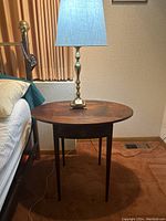 Pair of dark wood drop-leaf Pembroke end tables next to beds, showing table top, hinged leaves and single drawer with brass pull, as well as tapered legs.