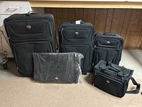 Photo of the entire 5-piece luggage set including 3 upright suitcases, duffel bag, and garment bag in front of a wooden background.