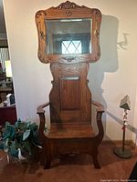 Front view of antique wooden hall tree showing carved top crest, beveled mirror and armrests with hooks.