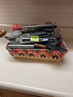 Overview photo showing the woven basket filled with assorted kitchen utensils, including tongs, whisk, spatula, and other tools.