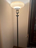Full view of a tall brass torchiere floor lamp showing the frosted glass shade illuminated and the slender brass pole.