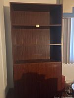 Front view of the tall cherry wood bookcase showing three open shelves and two closed cabinet doors below.