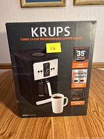 Front packaging box showing the KRUPS Turbo 12-Cup Programmable Coffee Maker with features listed including turbo function, strength intensity, customized brewing, and gold-tone filter.