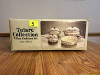 Photo of the front side of the box showing the Tulare Collection 7 Piece Cookware Set by Lake Forest with an image of the cookware set featuring floral pattern on cream background and solid brass handles.