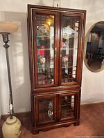 Full view of the dark cherry rosewood Chinese curio cabinet showing glass doors and shelves, intricate carving details, and polished wood.