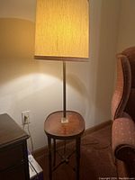 Photo showing the entire vintage floor lamp with cylindrical fabric lamp shade, slender metal pole and attached oval end table with faux wood finish.