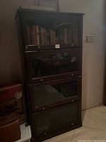 Front view of the dark wood barrister bookcase showing four glass-front door units stacked vertically containing books and items inside.