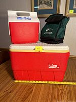 Photo showing all three items: large Igloo 25 ice chest, Igloo Mini Mate cooler, and green insulated lunch bag, placed on wooden floor.