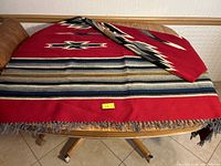 Large red handwoven wool throw blanket laid on table showing horizontal stripes and fringe