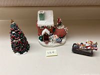 Photo displaying all three figurines: decorated Christmas tree, shoe-shaped musical house, and Santa on sleigh.