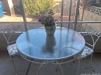 Full set showing the round glass table with white wrought iron frame and two matching cushioned chairs on a patio.