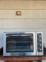 Front view of a KitchenAid stainless steel portable countertop oven with glass door and two wire racks visible inside, four control knobs on right side.