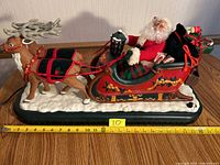 Side view showing Santa Claus holding reins in red sleigh with two reindeer, on white snow-like base, with measuring tape for size reference.