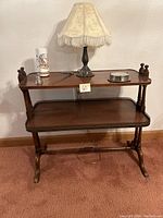 Front view of vintage mahogany two-tier side table with Victorian-style lamp, candle and snuffer, and coasters on top shelf.