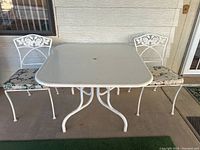 Full view of the white square metal patio table with two matching metal chairs, showing table dimensions and style.