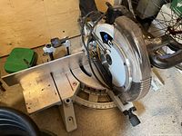 Side-angle photo showing the full base, blade guard, and handle of the Delta miter saw placed on the floor alongside other items.