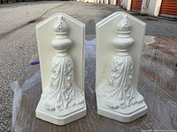 Pair of white painted cast iron bookends facing front showing leaf motif and finial design