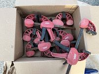 Top view of seven Skil wood bar clamps in a cardboard box showing red handles and black metal bars.