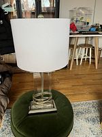 Photo of the contemporary glass table lamp showing the clear glass base with geometric circular design and the white drum shade on top.