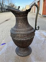 Front and side view of the large copper pitcher vase with detailed engraving and curved handle.