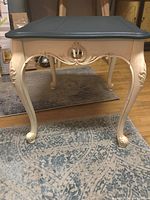 Front and side view of the Ethan Allen side table showing the dark blue-grey top, white painted body, decorative carvings on legs, and curved cabriole leg design.