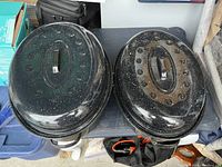 Top view of two vintage granite ware roaster pans with lids, one slightly larger than the other showing black finish with white speckles and vent holes on lids