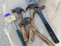 Top view of five hammers laid on cardboard background, showing four metal claw hammers with varying handle materials and one plastic mallet with a green handle.