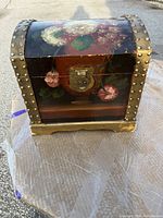 Photo of the closed wooden jewelry box showing front floral painting, brass lock, and decorative brass studs.
