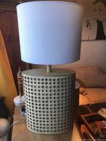 Full view of one lamp showing cylindrical perforated base and white drum shade on a wooden table near couch.