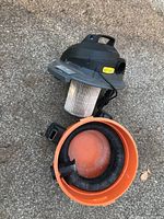 Top down view showing vacuum with filter exposed and hose coiled inside orange container.