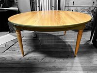 Photo of the round wooden table with a natural wood grain top and painted apron, showing leg detail and floor beneath.