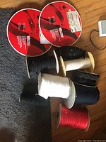 Photo showing multiple rolls of elastic in black, white, and red, black lace trim, black binding jersey fabric, and two large Velcro rolls with red labels.