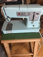 Full side view of Singer Model 348 sewing machine sitting on a wooden table with green mat underneath.