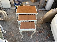 Three stacked wooden tables with scalloped edges and white painted cabriole legs in an outdoor setting.